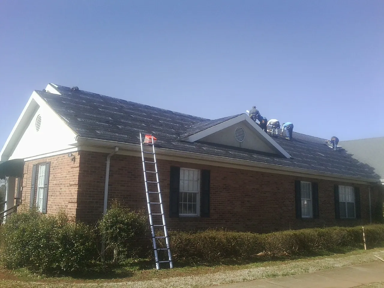 Crew tearing shingles off a brick ranch roof with a ladder set — Emergency Roof Repair work by our crew in Charleston Afb