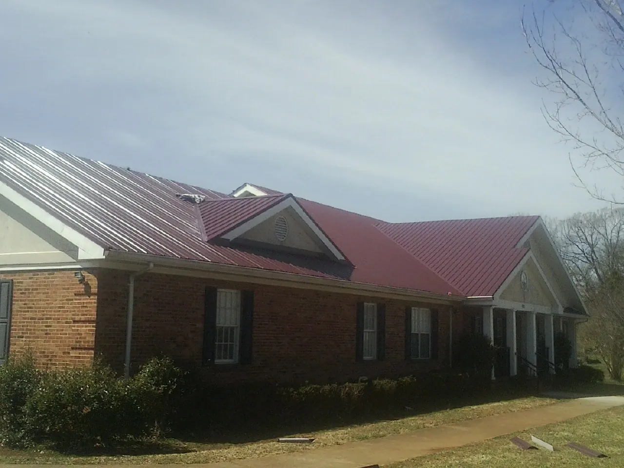 Red metal roof with gabled entries on a long brick building, from a Hail Damage Roof Repair job in Charleston Afb