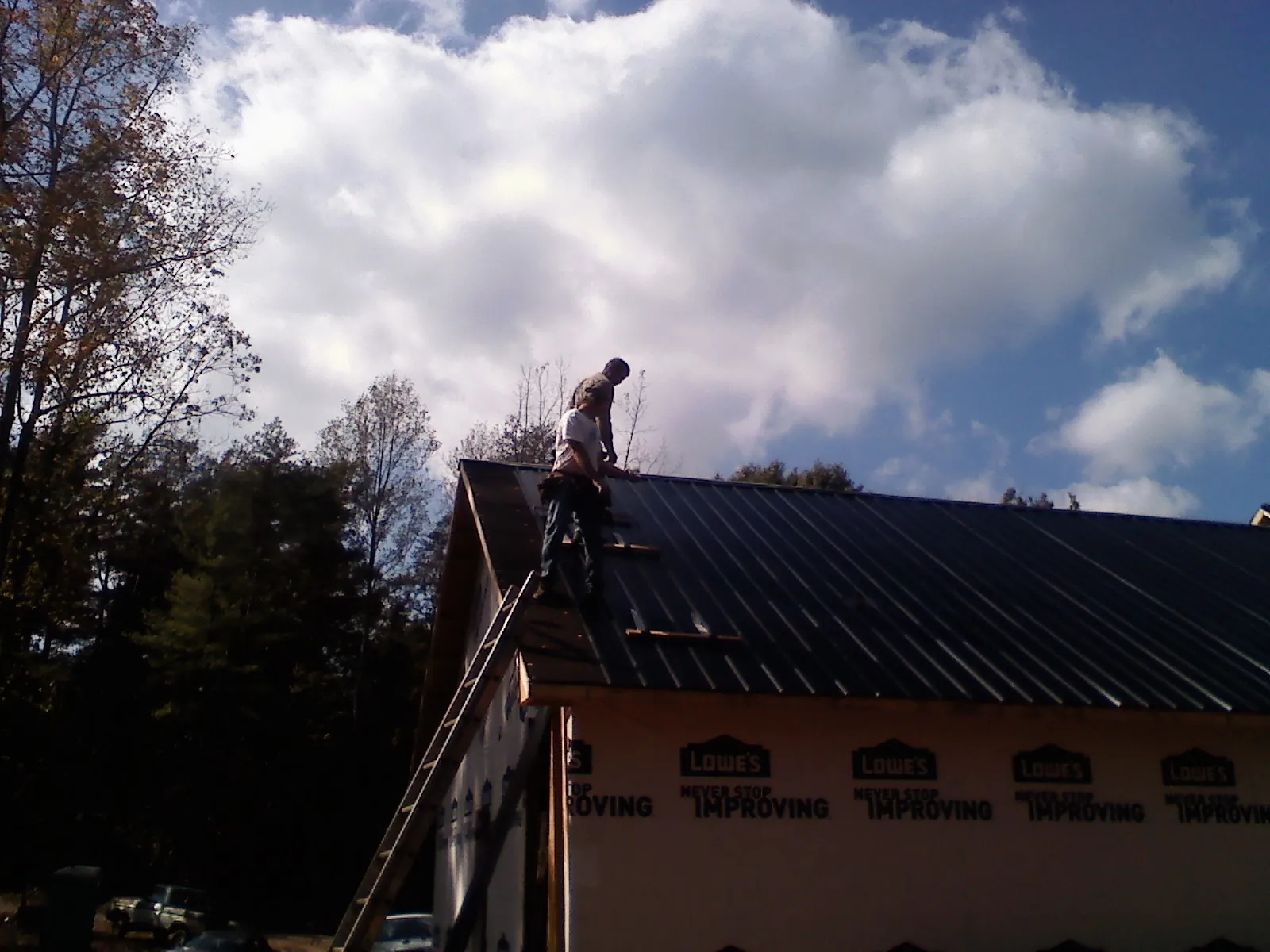 Roofer fastening dark metal panels high against a cloudy sky, from a Roof Inspection job in Charleston Afb