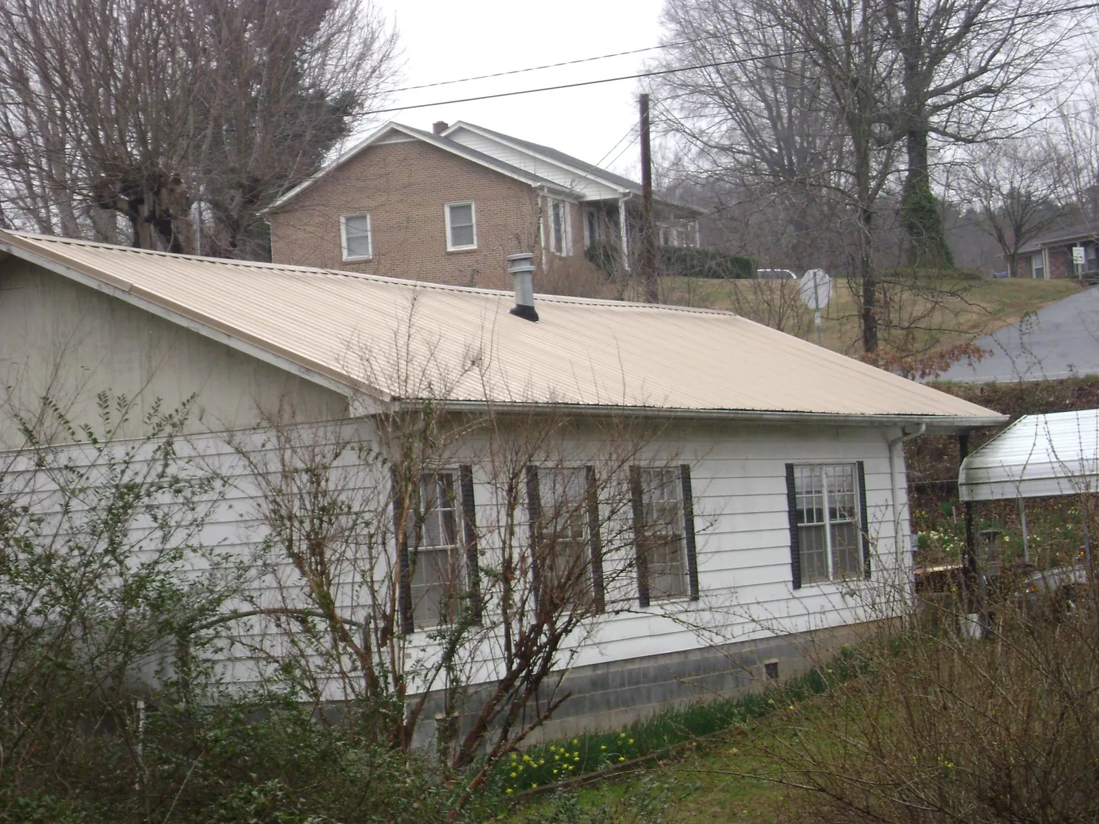 Tan metal roof on a white sided house set into a hillside — Commercial Roofing by Roofing Brothers in Charleston Afb